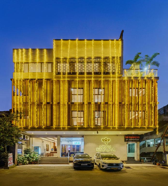 a yellow building with two cars parked in front of it at Hotel Kiyara in Kolhapur
