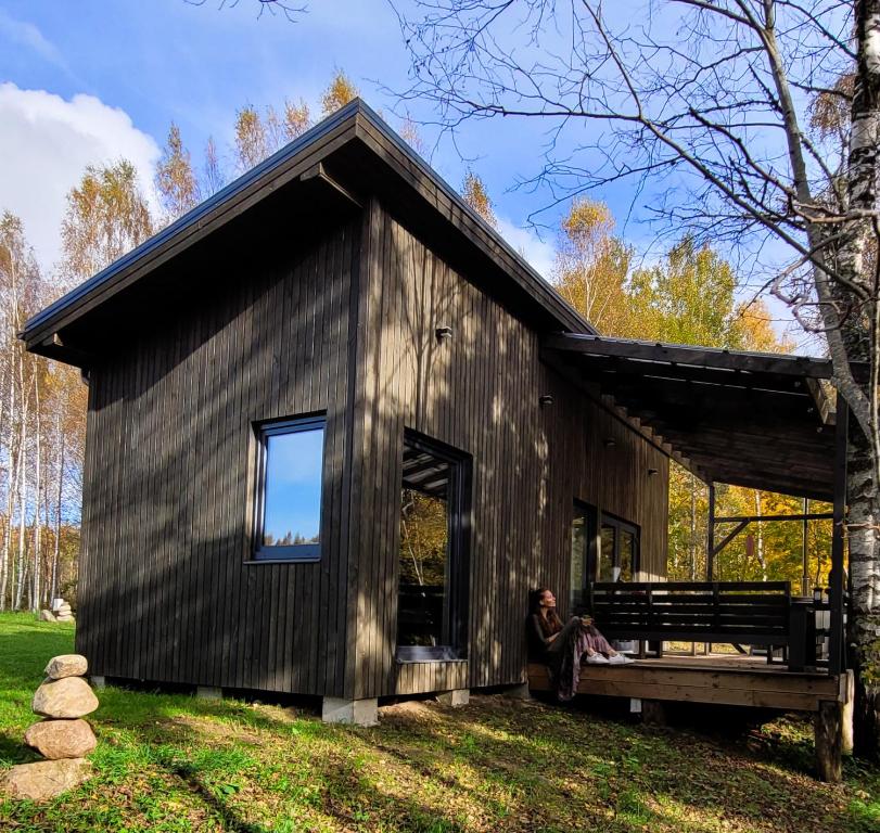 a person sitting on a bench in front of a house at Holiday cabin 'OAK' in Salacgrīva