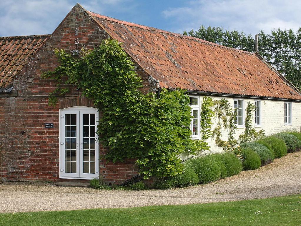 een stenen huis met een witte deur en klimop bij Valley Farm Cottage in Sudbourne
