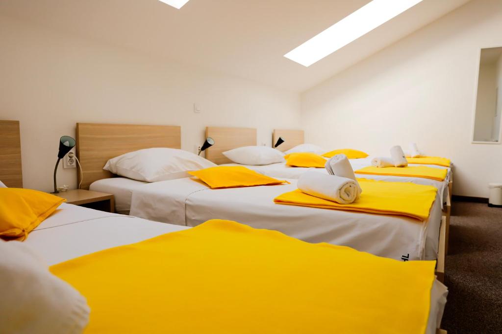 a room with three beds with yellow and white sheets at London Rooms Zagreb Airport in Velika Gorica
