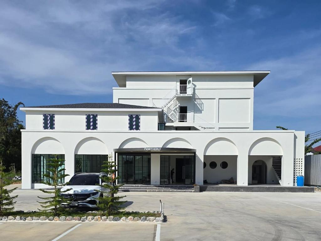 a white building with a car parked in a parking lot at Northerly นอร์ทเทอร์ลี่ in Chiang Rai