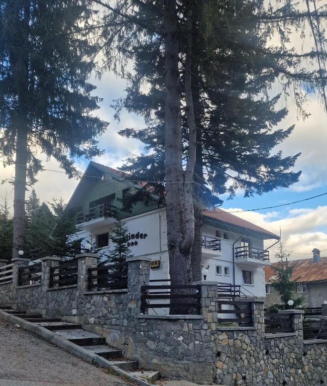 a white house with a tree and a stone wall at Pensiunea Kalinder in Buşteni