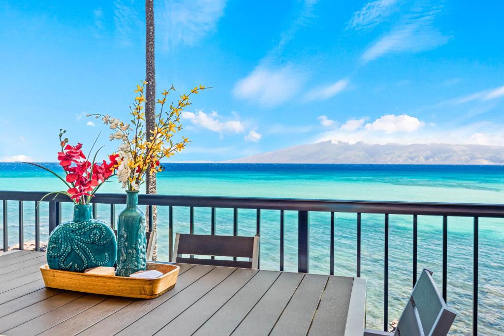 Noelani 302 في Kapalua-West Maui Airport: طاولة مع مزهرتين على شرفة مطلة على المحيط