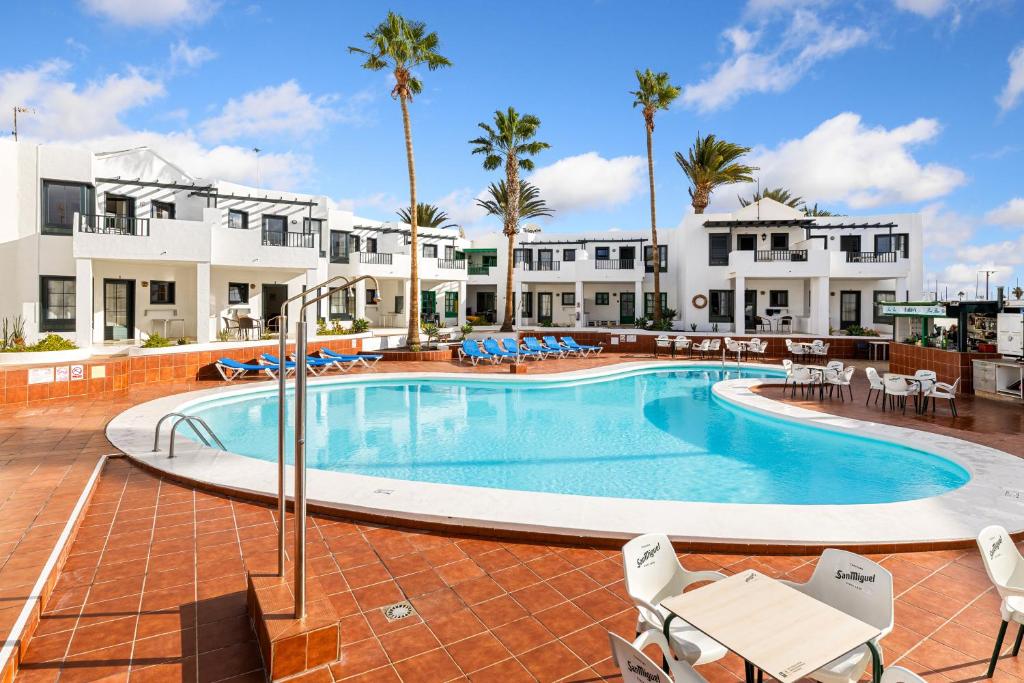 une piscine avec des chaises et des palmiers dans l'établissement Apartamentos Luz Y Mar, à Puerto del Carmen