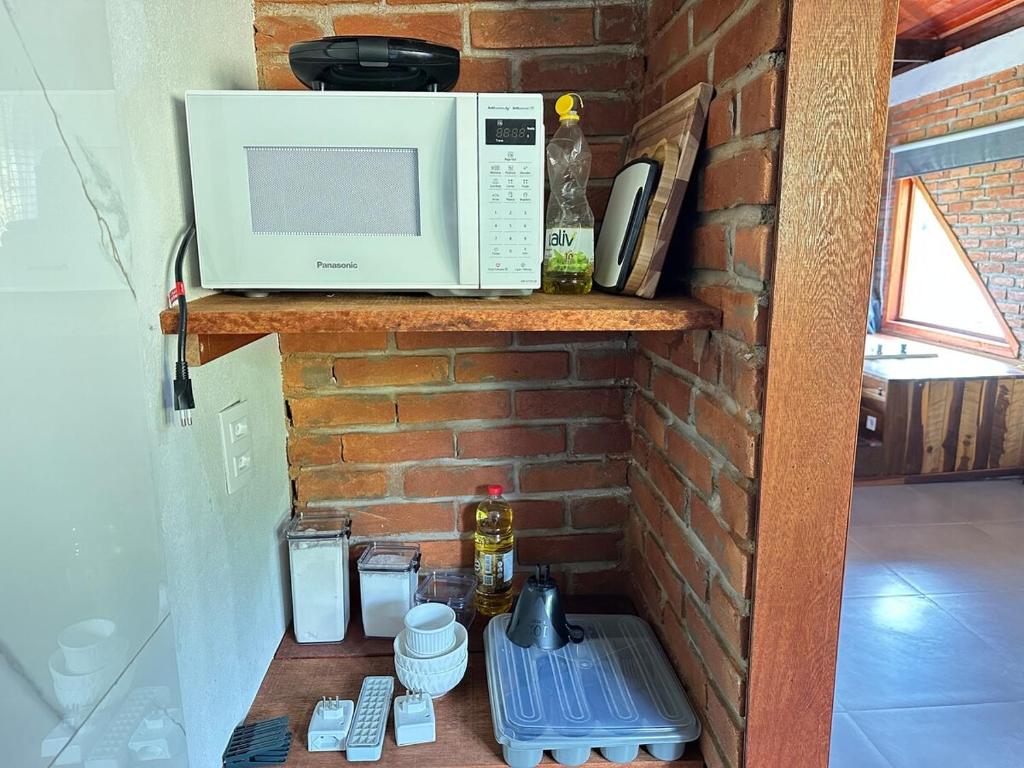eine Mikrowelle auf einem Regal neben einer Ziegelwand in der Unterkunft Chalés das Cachoeiras - Amor Perfeito in Resende