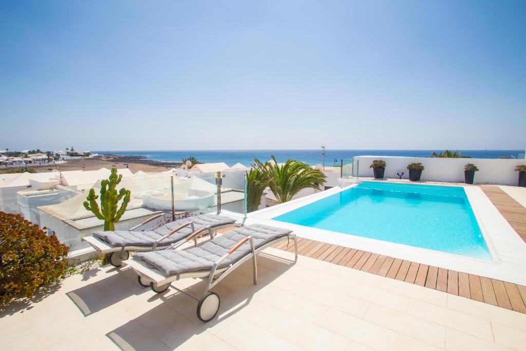 a swimming pool with two lounge chairs and the ocean at Alexia Beach in Playa Honda