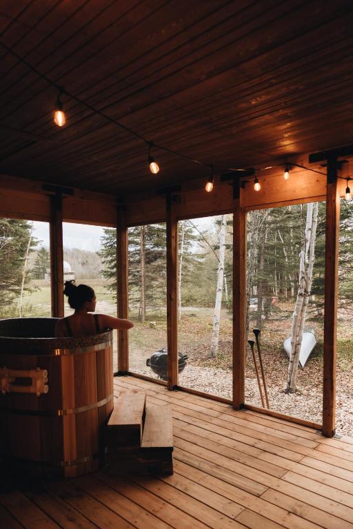 a woman sitting in a hot tub on a wooden deck at Micro-cabine, Méandre, La Tuque in La Tuque