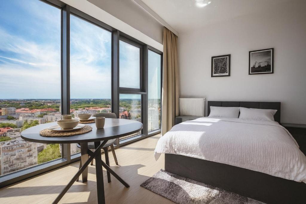 una camera da letto con un letto, un tavolo e grandi finestre di Luksusowy apartament z widokiem, basenem i sauną Hanza Tower a Stettino