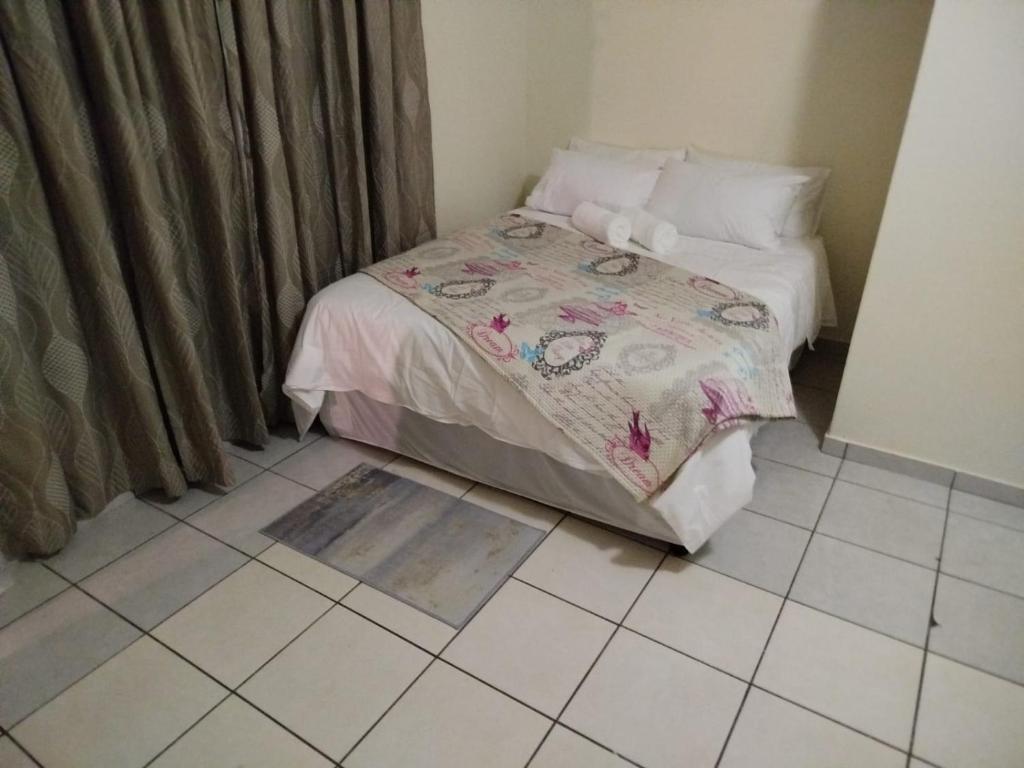 een kleine slaapkamer met een bed en een tegelvloer bij Manor Rentals in Potchefstroom