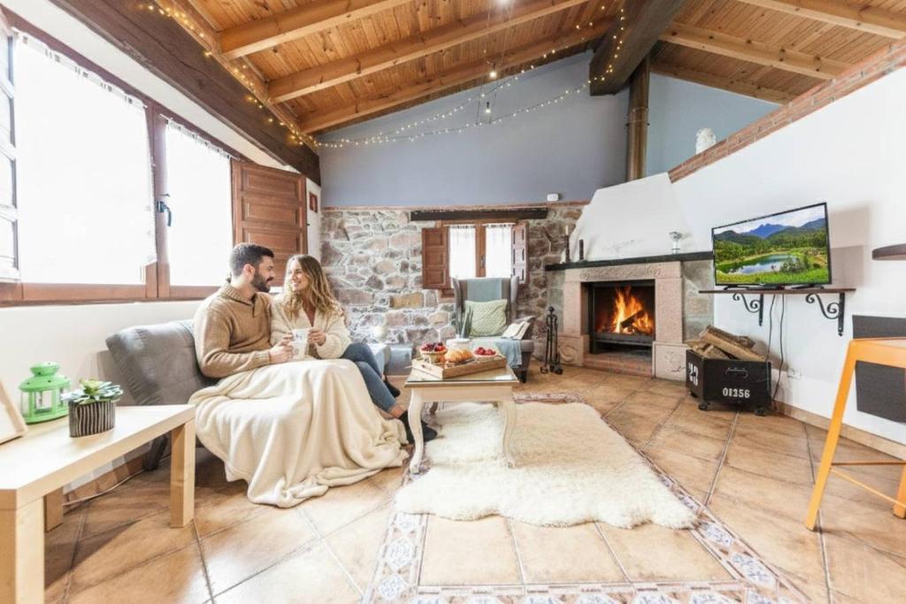 a couple sitting on a couch in a living room with a fireplace at Carbayu Senda del Oso in Proaza