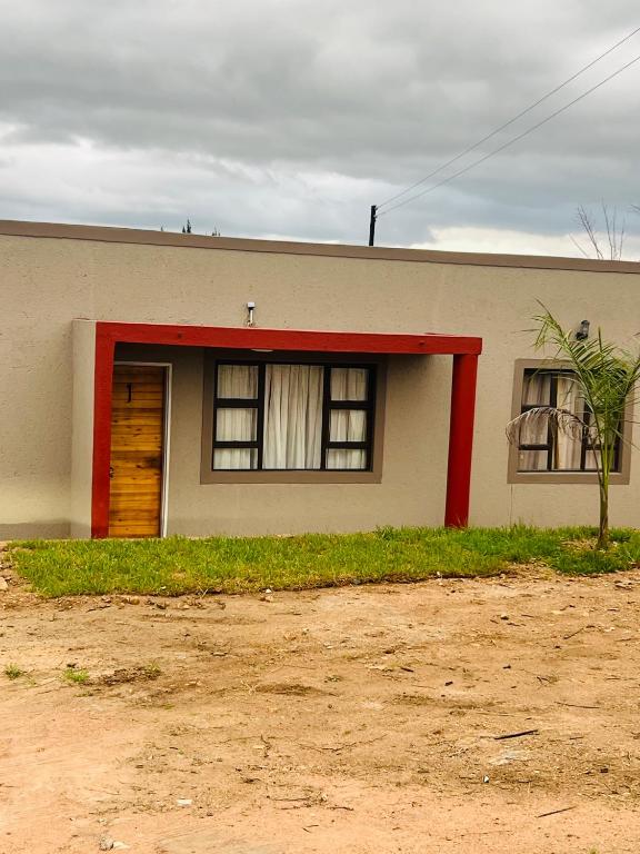 Emgwenyeni Guest house في منزيني: منزل فيه باب احمر و نافذتين
