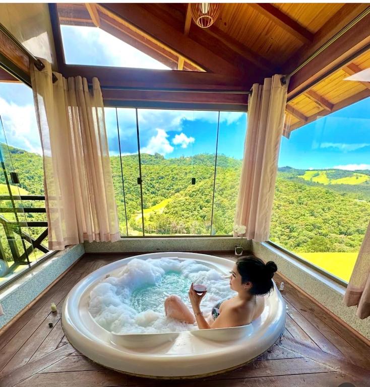 a woman sitting in a bath tub in a room with a window at Chalés Recanto Vista do Valle in Monte Verde