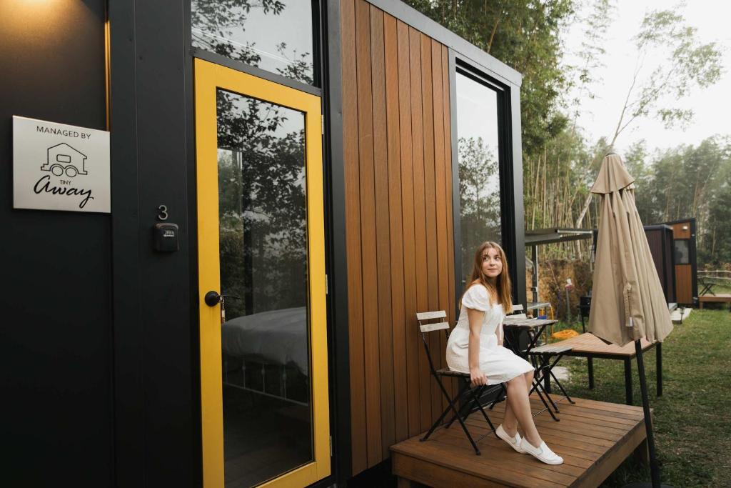 Una mujer sentada en una silla afuera de una pequeña casa. en Ninekm Forest Wilderness X by Tiny Away, en Wufeng