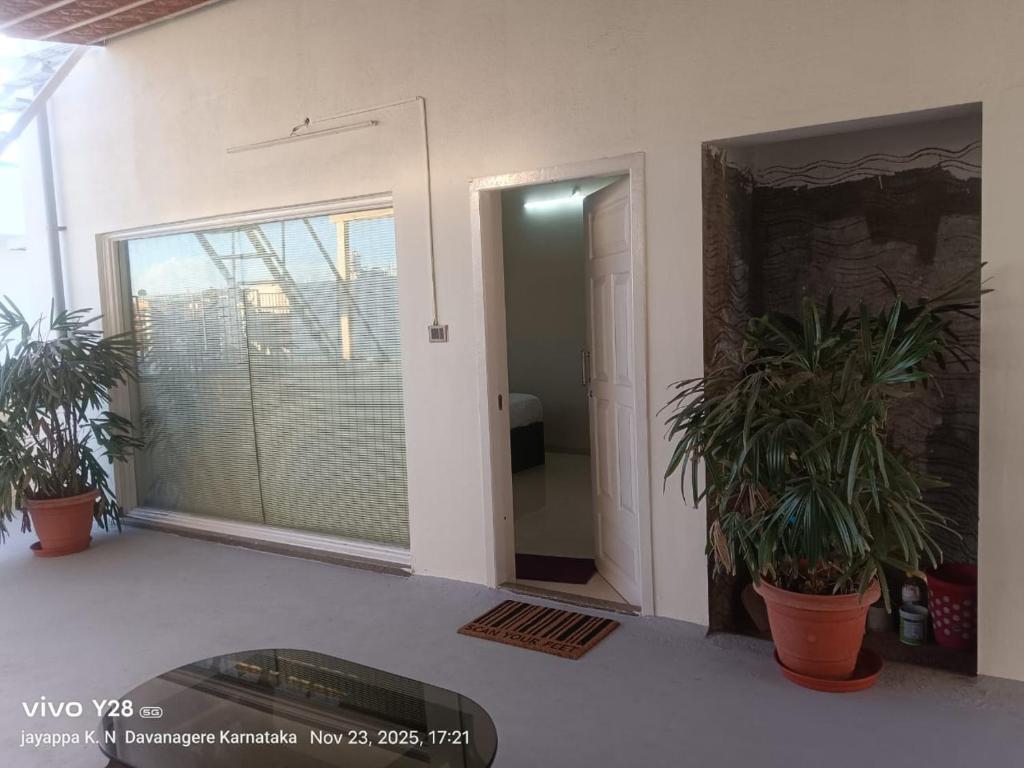Zimmer mit Topfpflanzen und Glastür in der Unterkunft Aakruthi Homestay in Davanagere