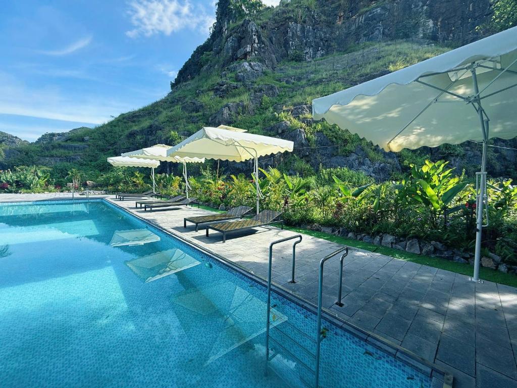 ein Swimmingpool mit Stühlen und Sonnenschirmen neben einem Berg in der Unterkunft Trang An River Sunshine Bungalow in Xuân Sơn
