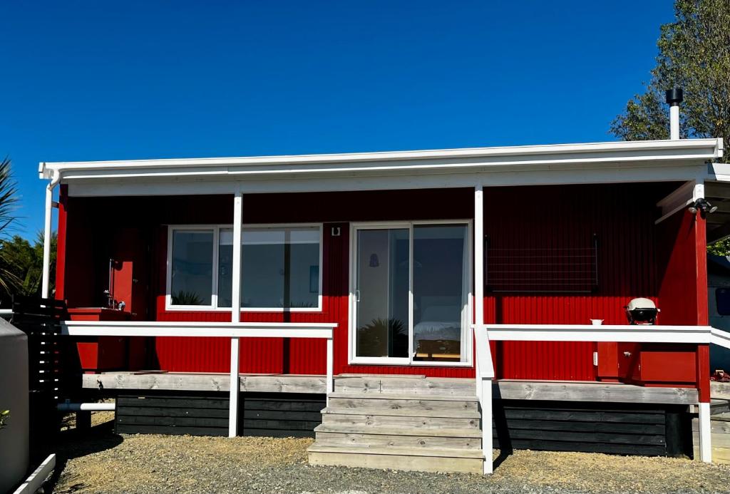 een rood huis met een rode deur en witte kozijnen bij Redshed Studio Mangawhai in Mangawhai