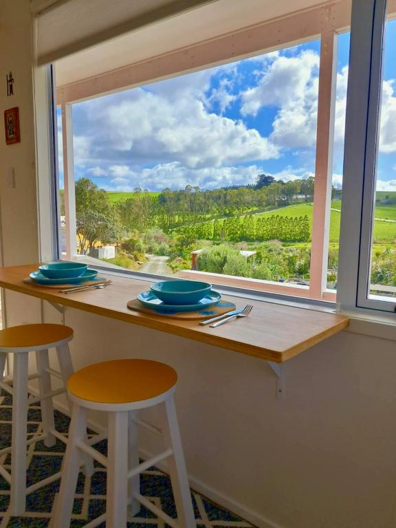 a table with two stools and a large window at Redshed Studio Mangawhai in Mangawhai