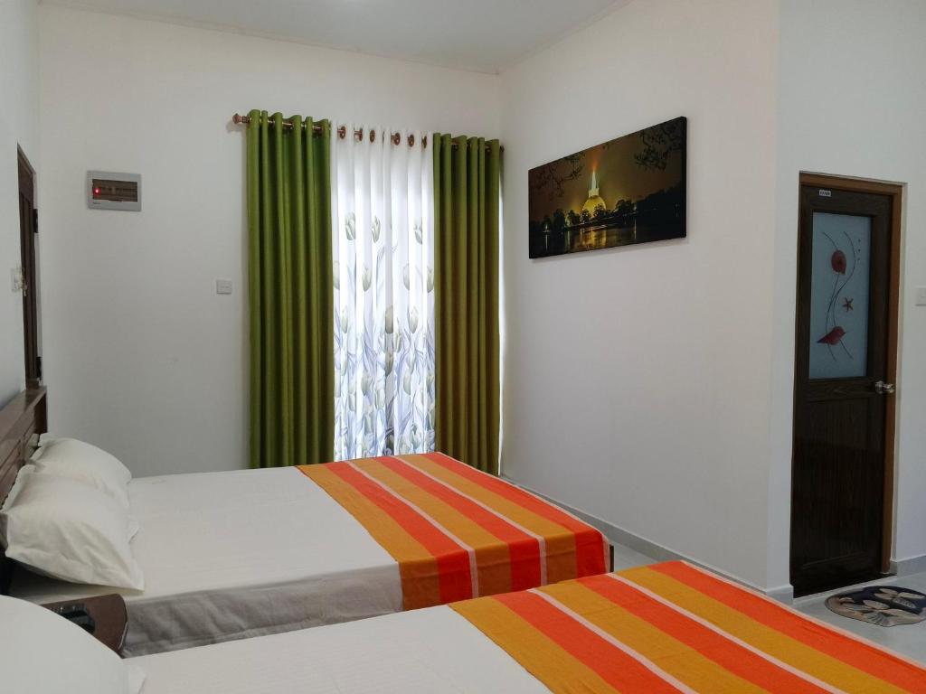 a bedroom with two beds and a window with green curtains at Didula Holiday Resort Anuradhapura in Anuradhapura