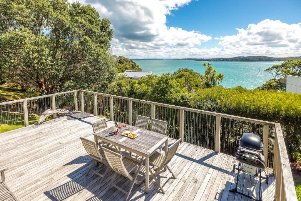a table and chairs on a deck with a view of the water at Black Cottage - Stay Waiheke in Waiheke Island