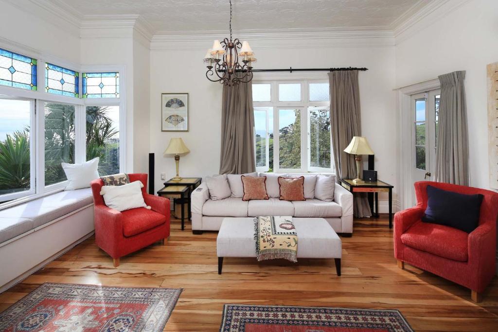 Crescent Villa - Stay Waiheke في Ostend: غرفة معيشة مع كراسي حمراء وأريكة بيضاء