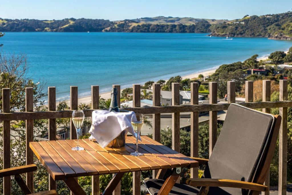 a wooden table with a bottle of wine and two glasses at Wavesong - Stay Waiheke in Onetangi