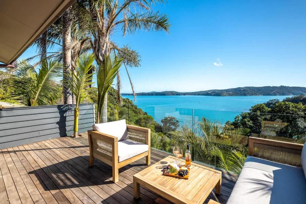 een terras met een tafel en een stoel en uitzicht op het water bij Palms on Kennedy Point - Stay Waiheke in Te Whau Bay