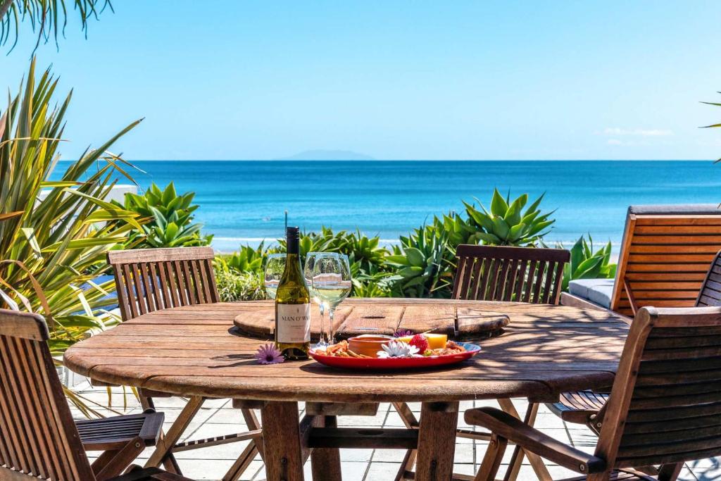 a wooden table with a bottle of wine on the beach at The Sands - Villa 28 - Stay Waiheke in Onetangi