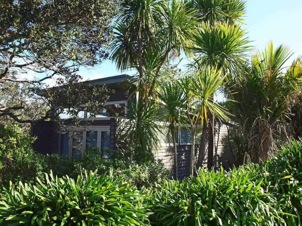 a house surrounded by palm trees and bushes at Tutiri in Oneroa - Stay Waiheke in Oneroa