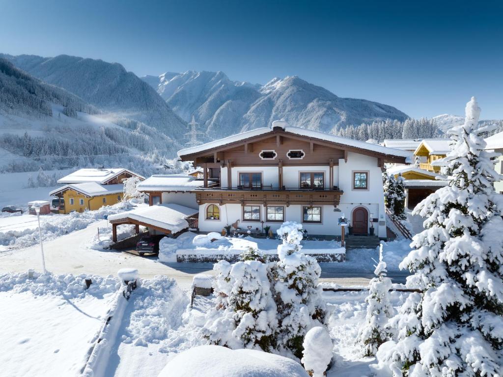 a house in the snow with mountains in the background at Gästehaus Stotter in Neukirchen am Großvenediger