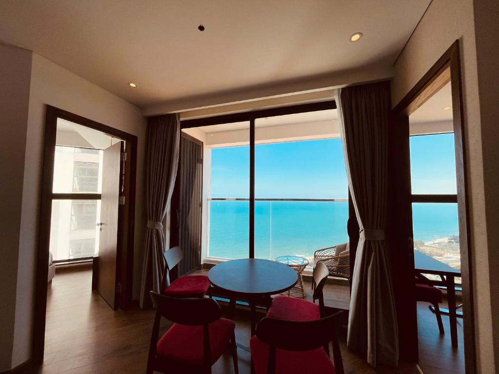 Zimmer mit einem Tisch, Stühlen und großen Fenstern in der Unterkunft Minh Tân Apartment Mandala in Mui Ne