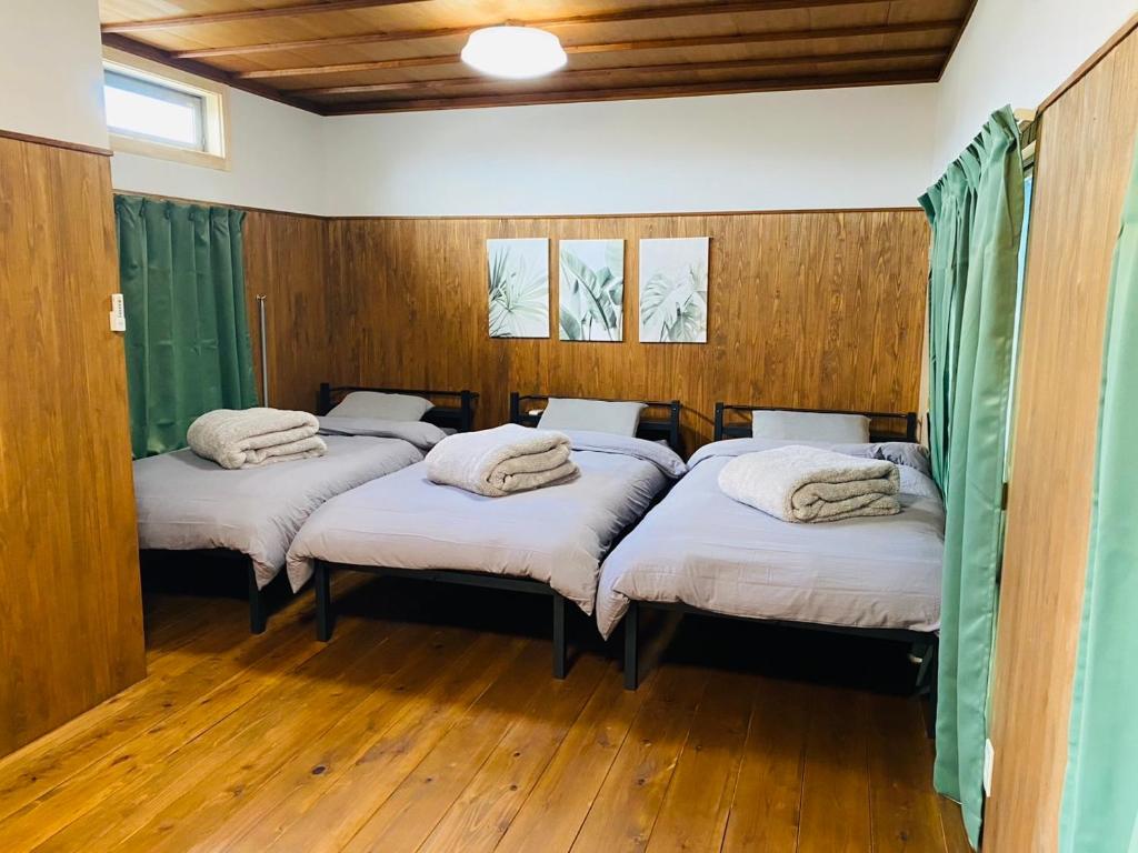 松山一棟貸し宿Tsuji في ماتسوياما: ثلاثة أسرة في غرفة مع ألواح خشبية