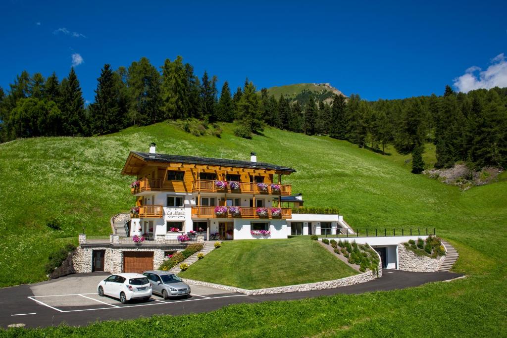 a house on a hill with two cars parked in a parking lot at Apartments La Mana in Santa Cristina Gherdëina