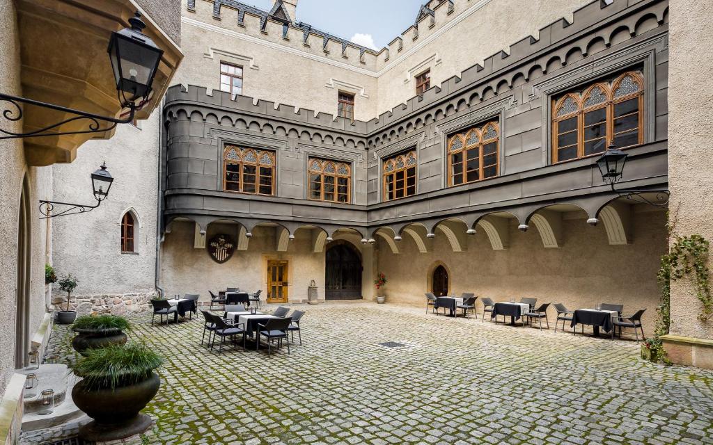 Quiet cobbled castle courtyard with scattered outdoor tables and chairs, arched gallery and wall lanterns