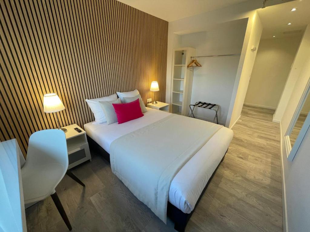 a bedroom with a large white bed and a chair at Hôtel les Coulisses in Forbach