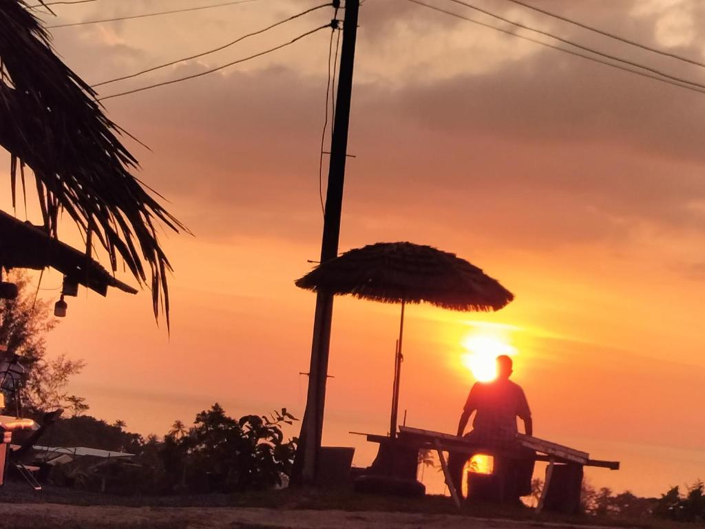 a person sitting at a picnic table with the sunset in the background at Shah Hill Hut in Phra Ae beach
