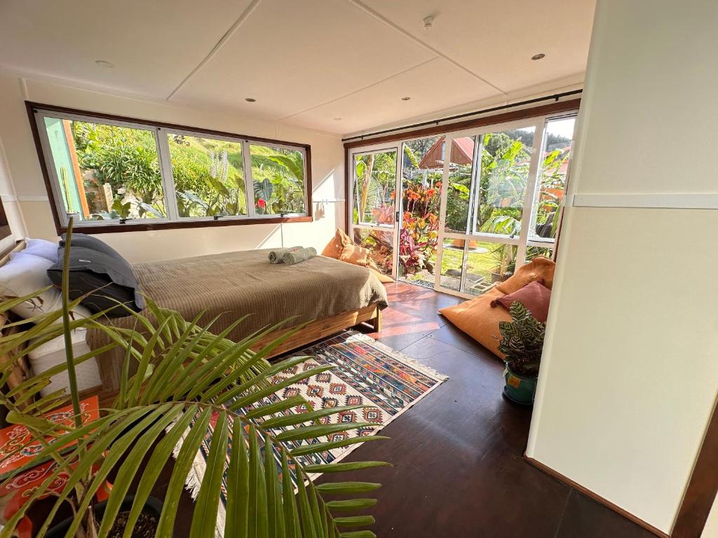 a bedroom with a bed and large windows at Pandora Cottage Beachfront in Raglan