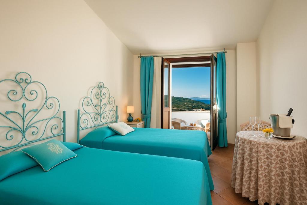 a hotel room with two blue beds and a window at Hotiday Baja Sardinia Saline in Cala Bitta