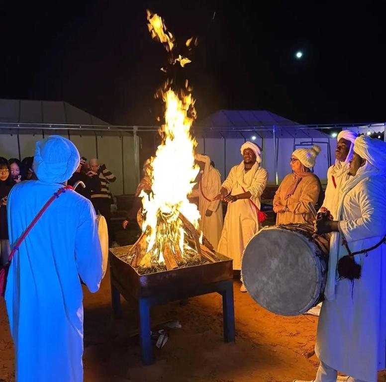 a group of people standing around a fire at Desert Pearl Camp in Merzouga