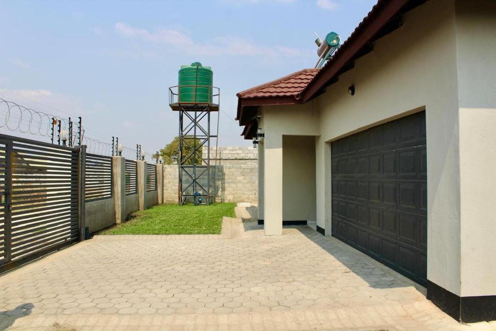 a house with a fence and a garage with a water tower at LOMS Furnished Apartment - Luxurious Modern House near KKI Airport in Kenneth Kaunda International Airport