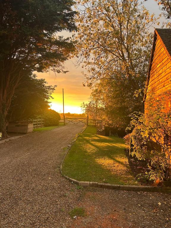 a road next to a barn with the sunset in the background at Country Cottage with moat in Ingatestone