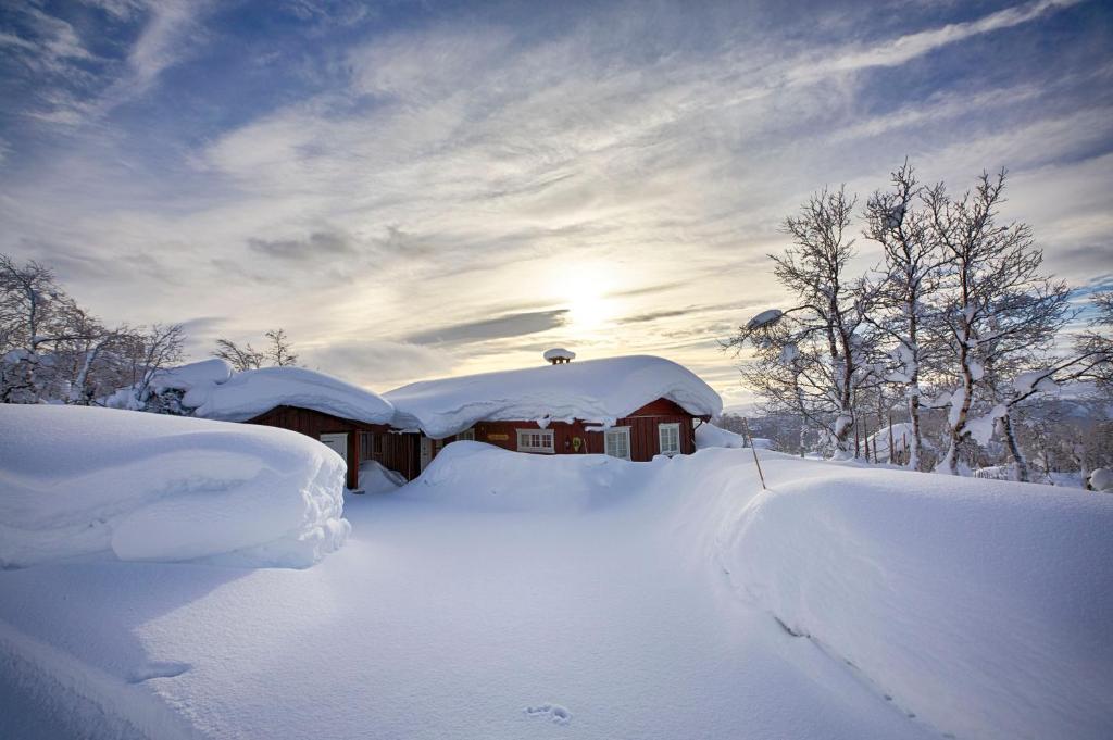 a house covered in snow with the sun in the background at Welcoming Cabin With Fireplace & Modern Kitchen in Beitostøl