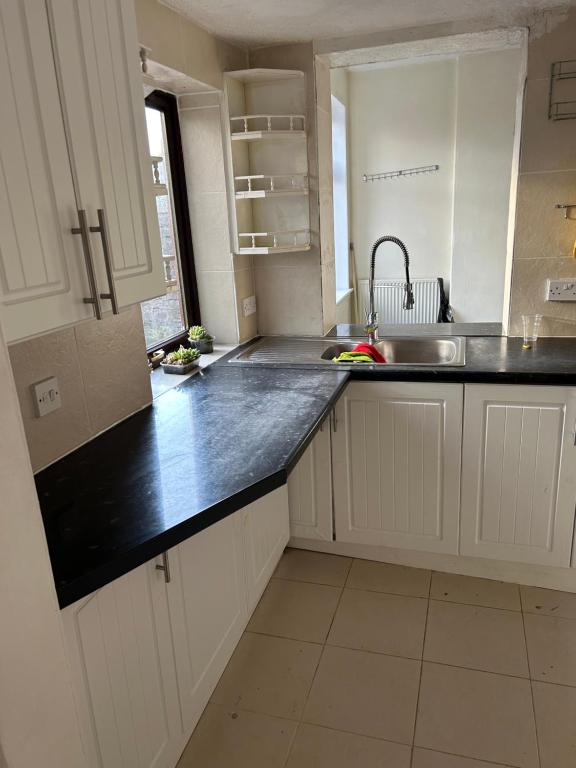 uma cozinha com armários brancos e uma bancada preta em Cozy & Comfy Apartments Dundee em Dundee