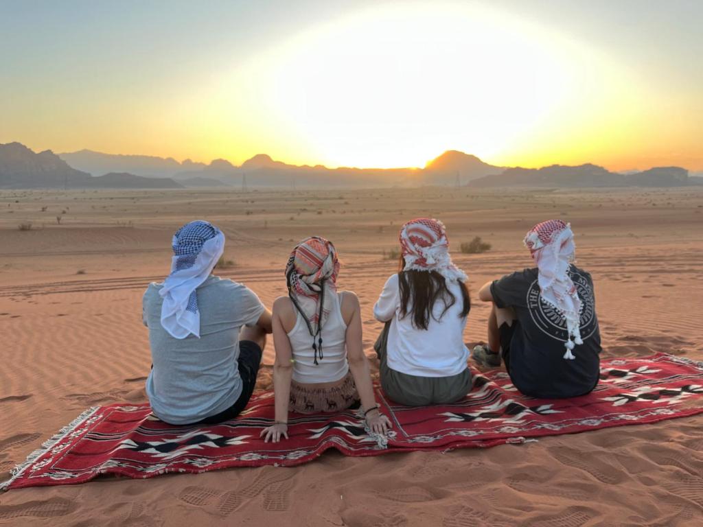 Quatro garotas sentadas no deserto observando o pôr do sol. em Malak rum camp em Wadi Rum