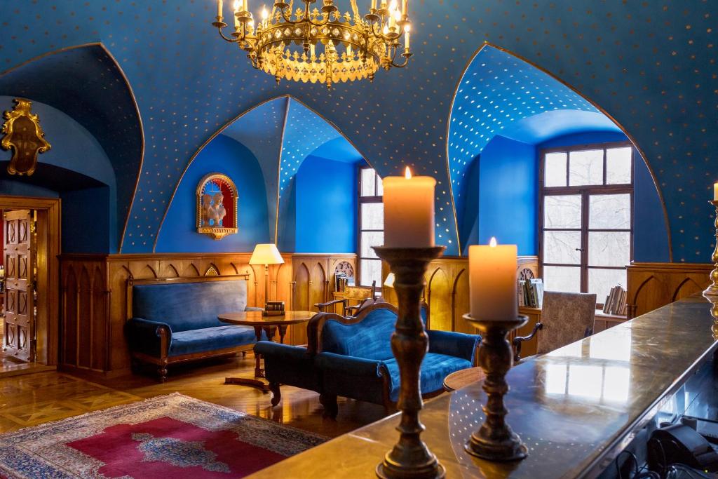Blue vaulted lounge with gold chandelier, lit candles in foreground and velvet sofas by arched windows, serene mood