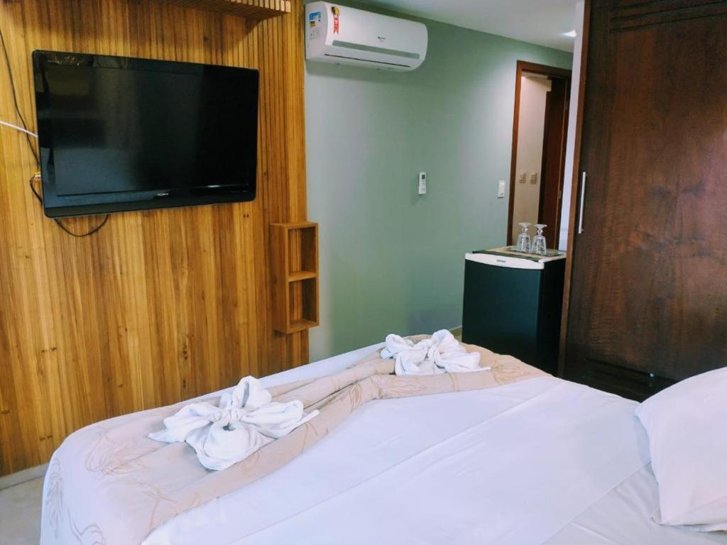 um quarto com uma cama branca e uma televisão de ecrã plano em Suíte Beleza do amor V11 A em Pipa