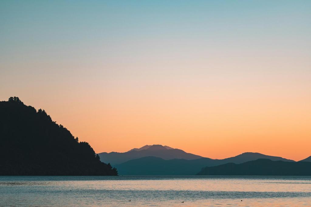 a sunset over the water with mountains in the background at Iconic Taupō Views in Taupo