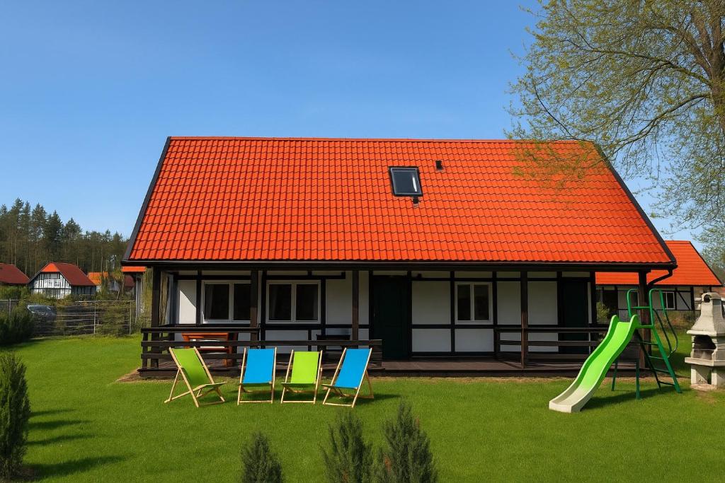 Kaszëbsko Nórcëk 8-10 osób 4 sypialnie jezioro las park linowy łowisko wędkarskie في Załakowo: منزل ذو سقف برتقالي اللون مزود بكراسي وملعب