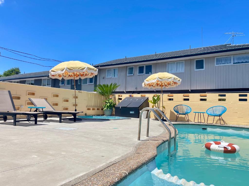 Mount Eden Motel في أوكلاند: مسبح مع مظلات وكراسي ومبنى