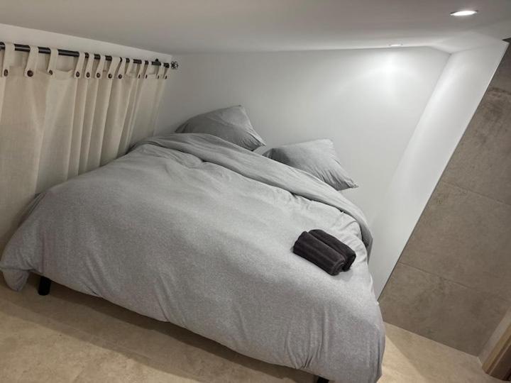 ein Bett in einem weißen Schlafzimmer mit einer schwarzen Tasche darauf in der Unterkunft Gîtes Vosges, Spa, Sauna & Piscine in Moyenmoutier