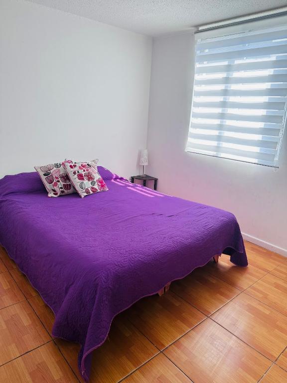 Departamento Playa Dichato في تومي: سرير أرجواني في غرفة بيضاء مع نافذة
